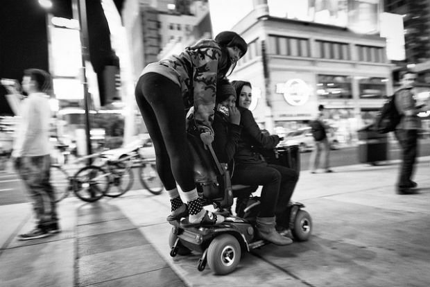 2 filles se déplacent avec un fauteuil roulant dans la ville